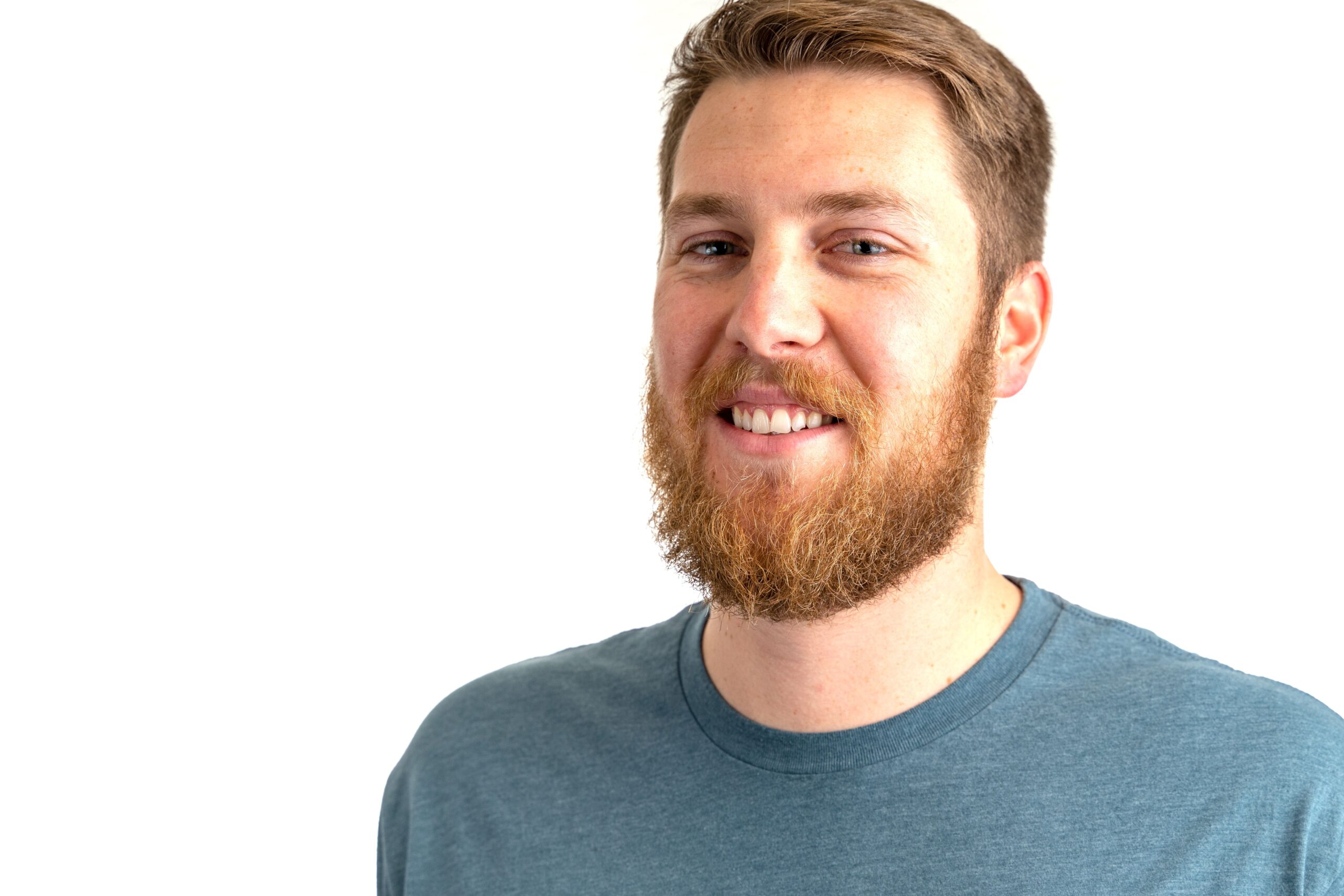 Close-up of a smiling bearded man in a casual blue shirt against a white background.